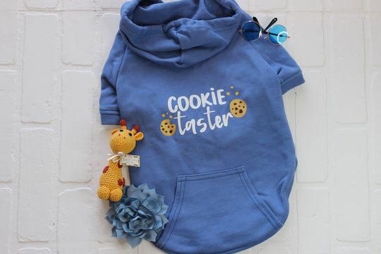 This blue dog hoodie has cookie taster in white vinyl letters with two chocolate chip cookies.